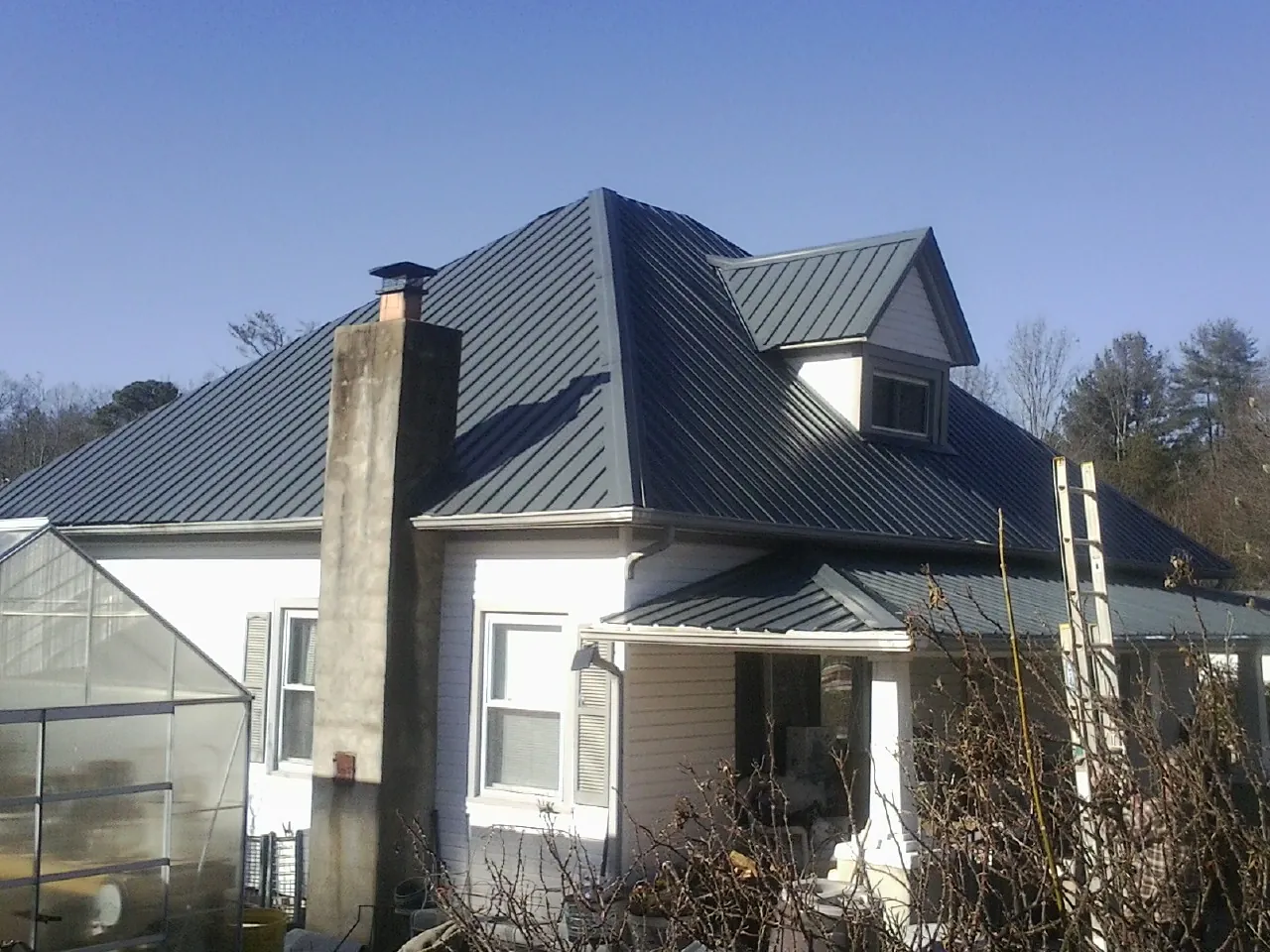 Dark blue standing seam metal roof on a white farmhouse with dormer — Slate & Tile Roof Repair by Roofing Brothers in High Point