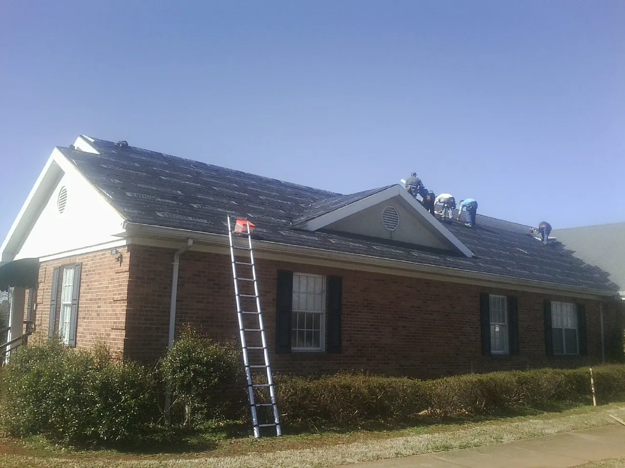 Crew tearing shingles off a brick ranch roof with a ladder set — Metal Roof Repair work by our crew in High Point