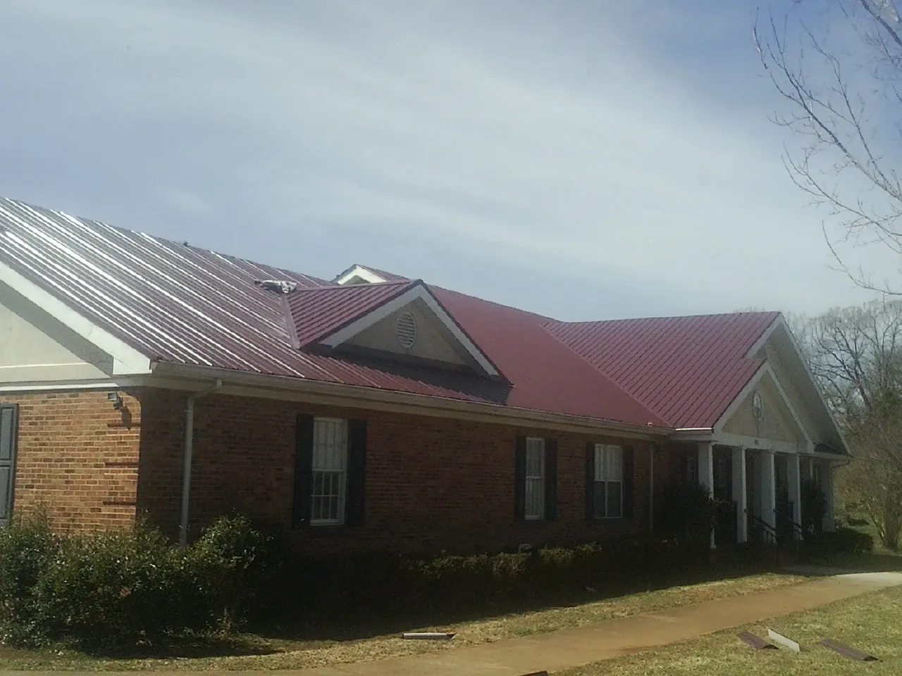 Red metal roof with gabled entries on a long brick building, from a Hail Damage Roof Repair job in High Point