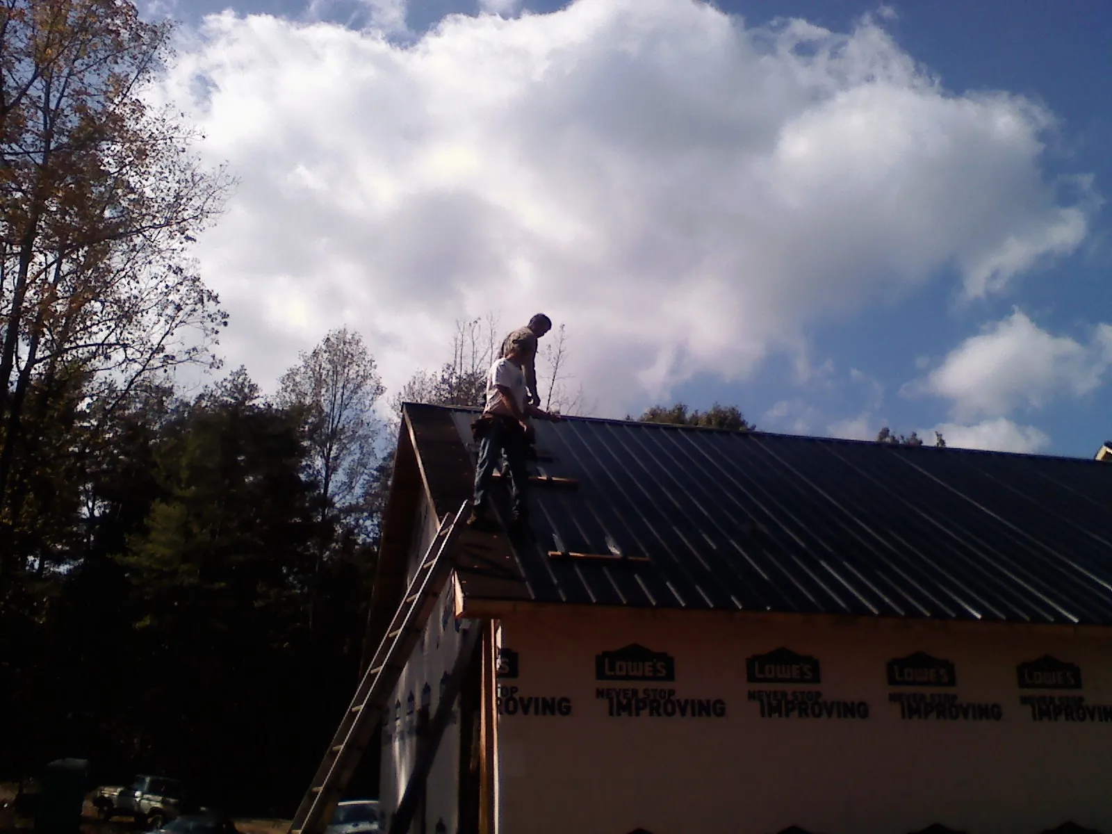Roofer fastening dark metal panels high against a cloudy sky, from a Roof Inspection job in High Point